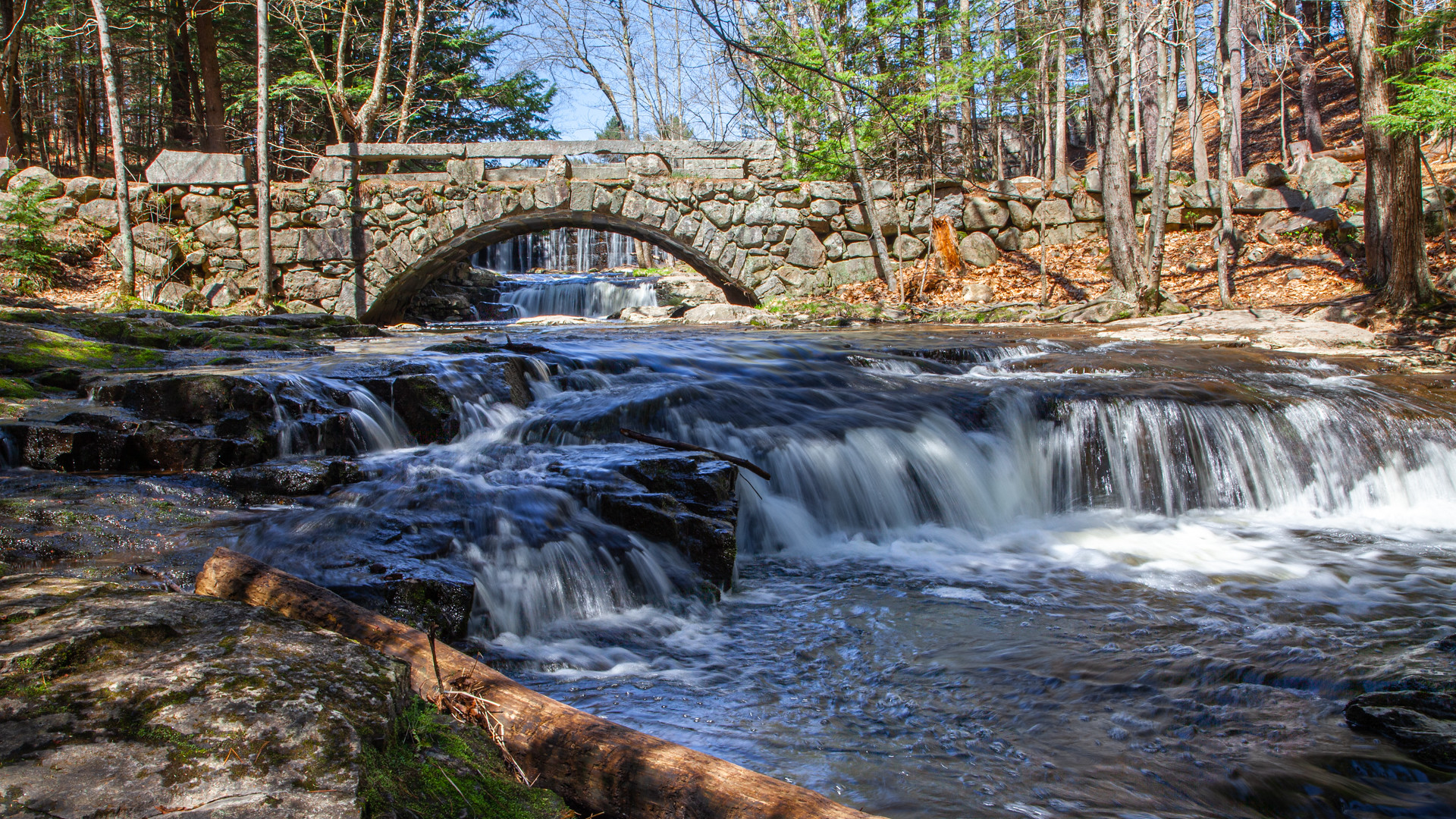 long exposure shot of a waterfall flowing under a cobblestone arch bridge in Maine.
