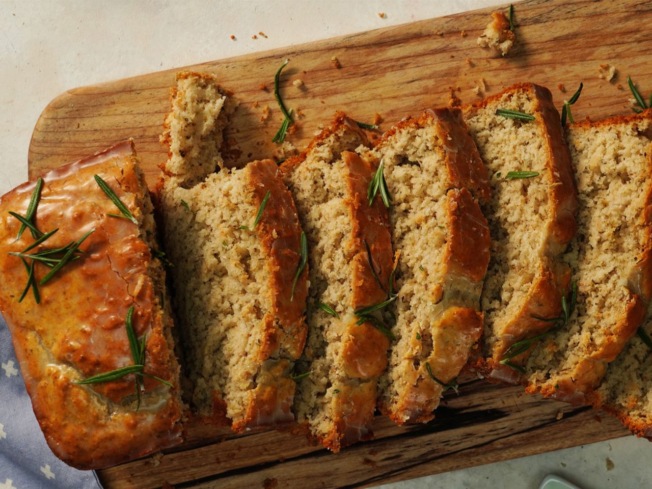 rosemary-garlic beer bread sliced on a cutting board and topped with fresh rosemary