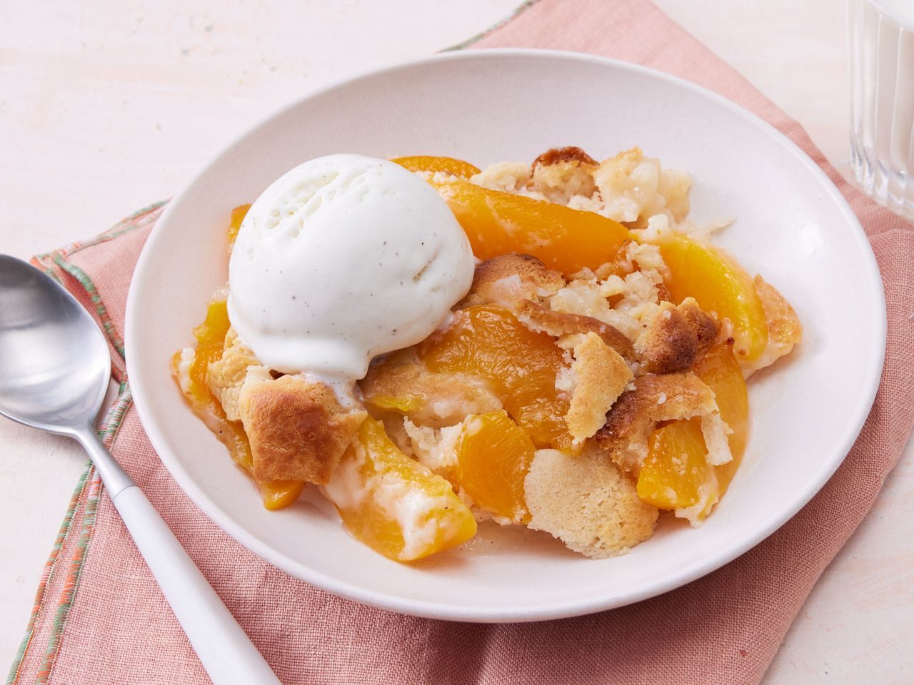 A bowl of classic Bisquick peach cobbler topped with vanilla ice cream