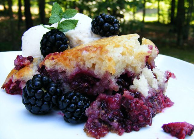 Blackberry cobbler garnished with raw blackberries, a mint sprig, and a scoop of vanilla ice cream