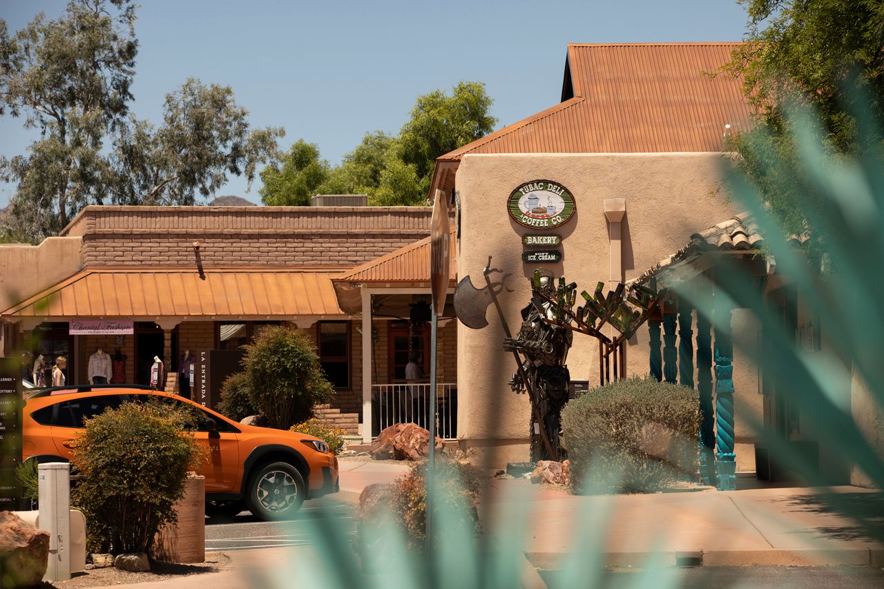 A view of a street with buildings and a statue featuring an orange vehicle in the foreground and desert surroundings