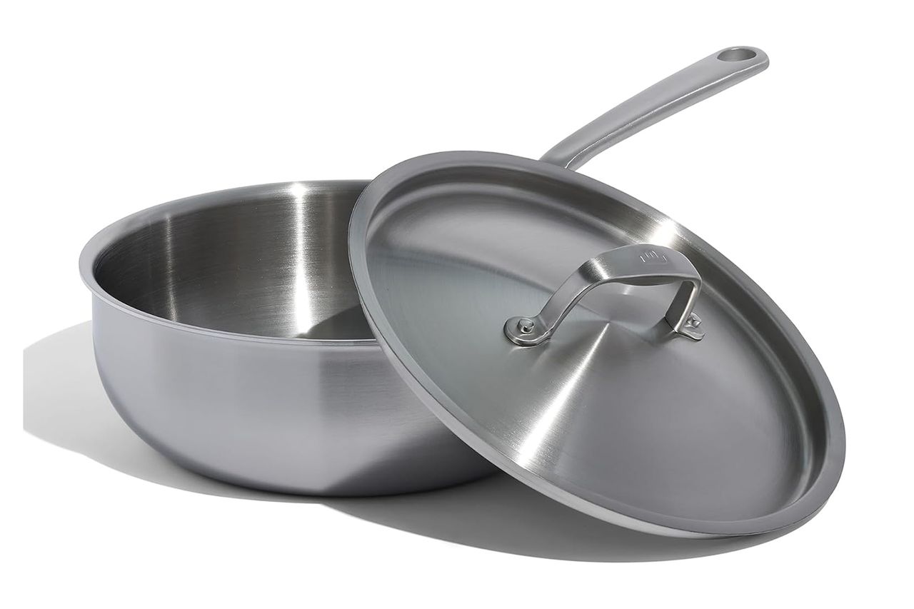 A metal saut pan with a matching lid slightly askew made of stainless steel