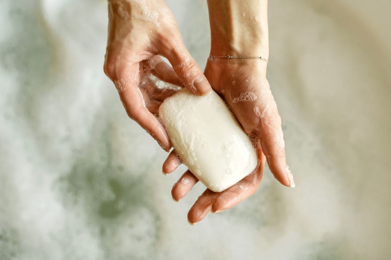 Hands holding a bar of soap over sudsy water closeup view