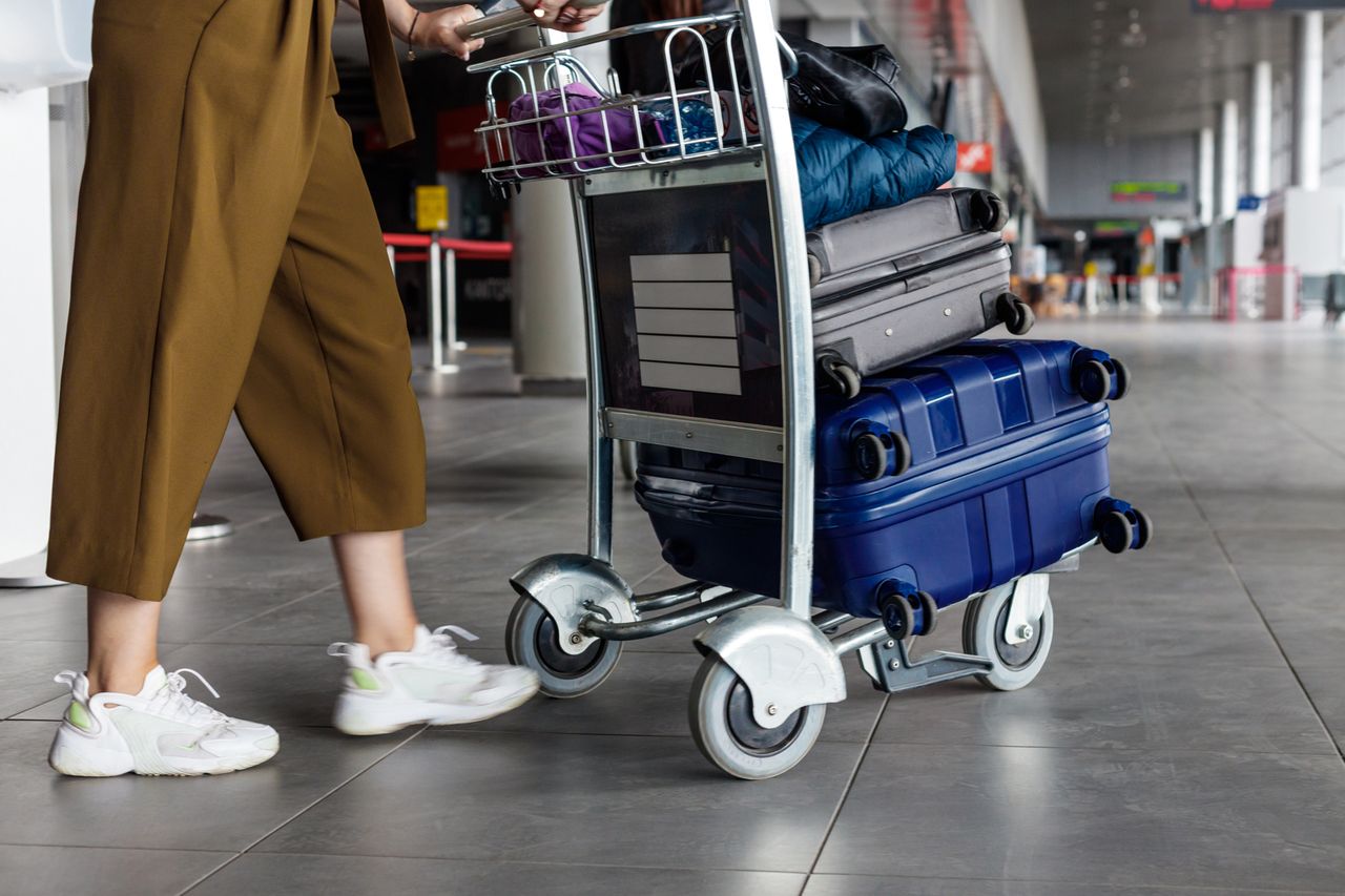 A person pushing a luggage cart with multiple suitcases in an airport setting