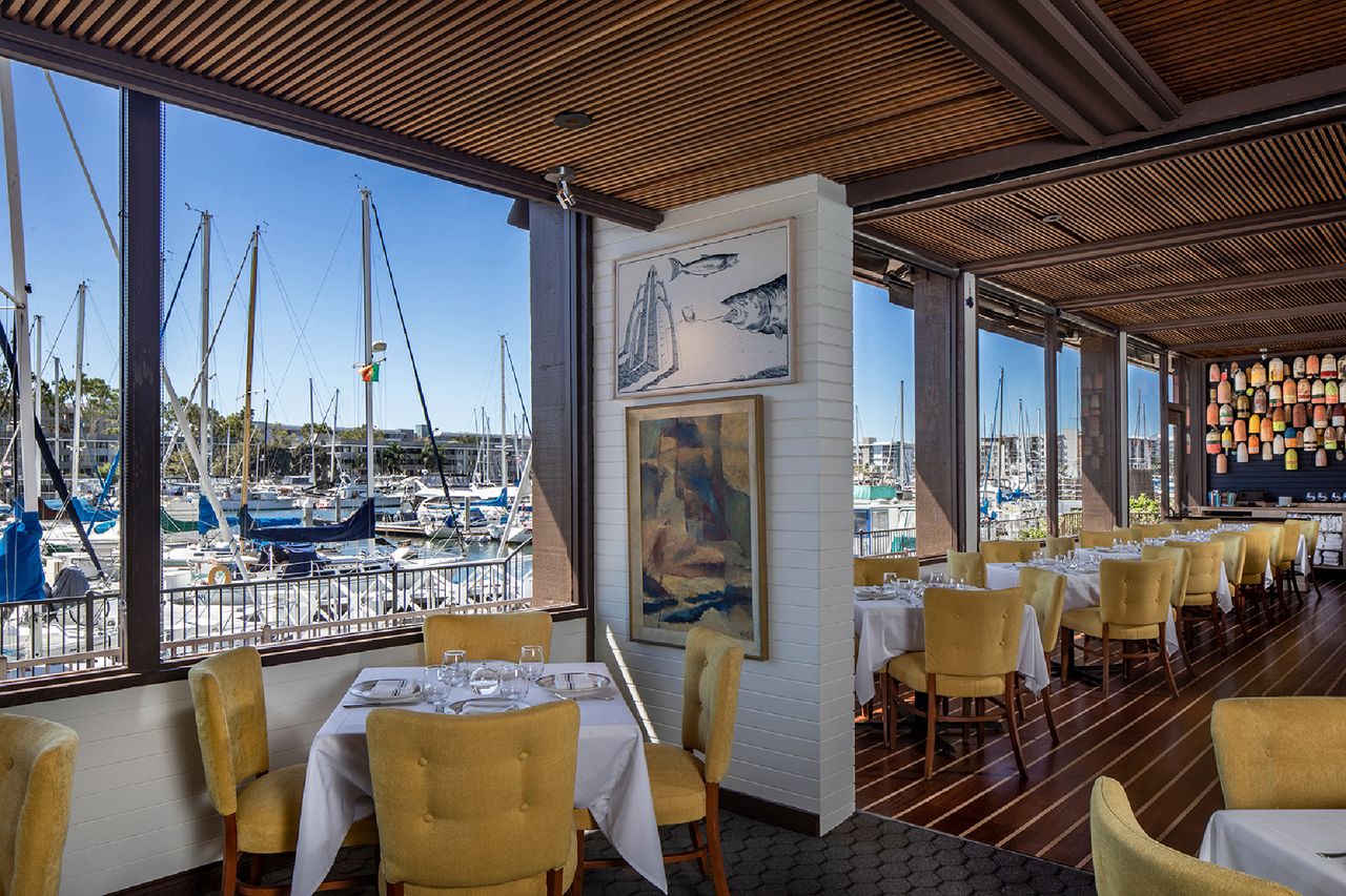 Restaurant interior with marina views through large windows white tablecloths on dining tables and paintings on the walls