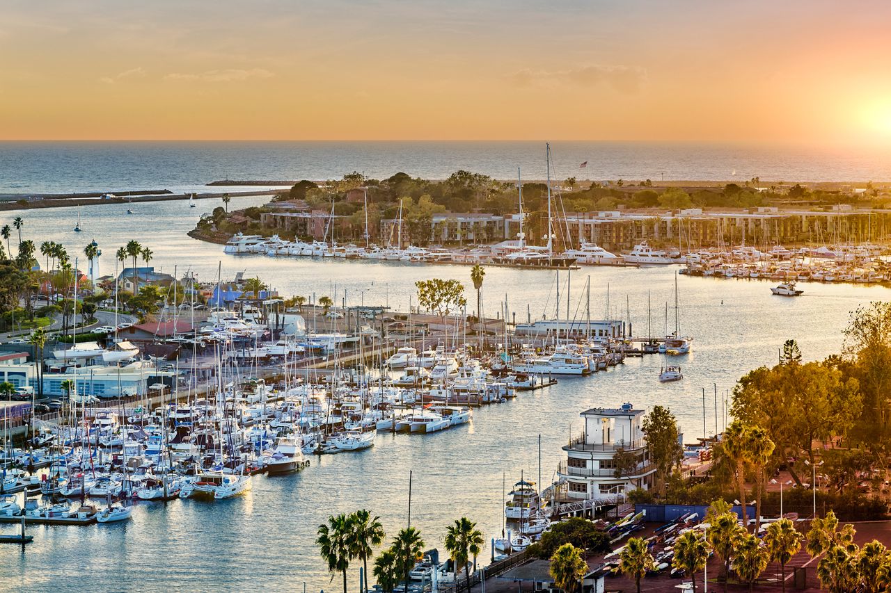 A marina with numerous docked boats and a sun setting on the horizon over water