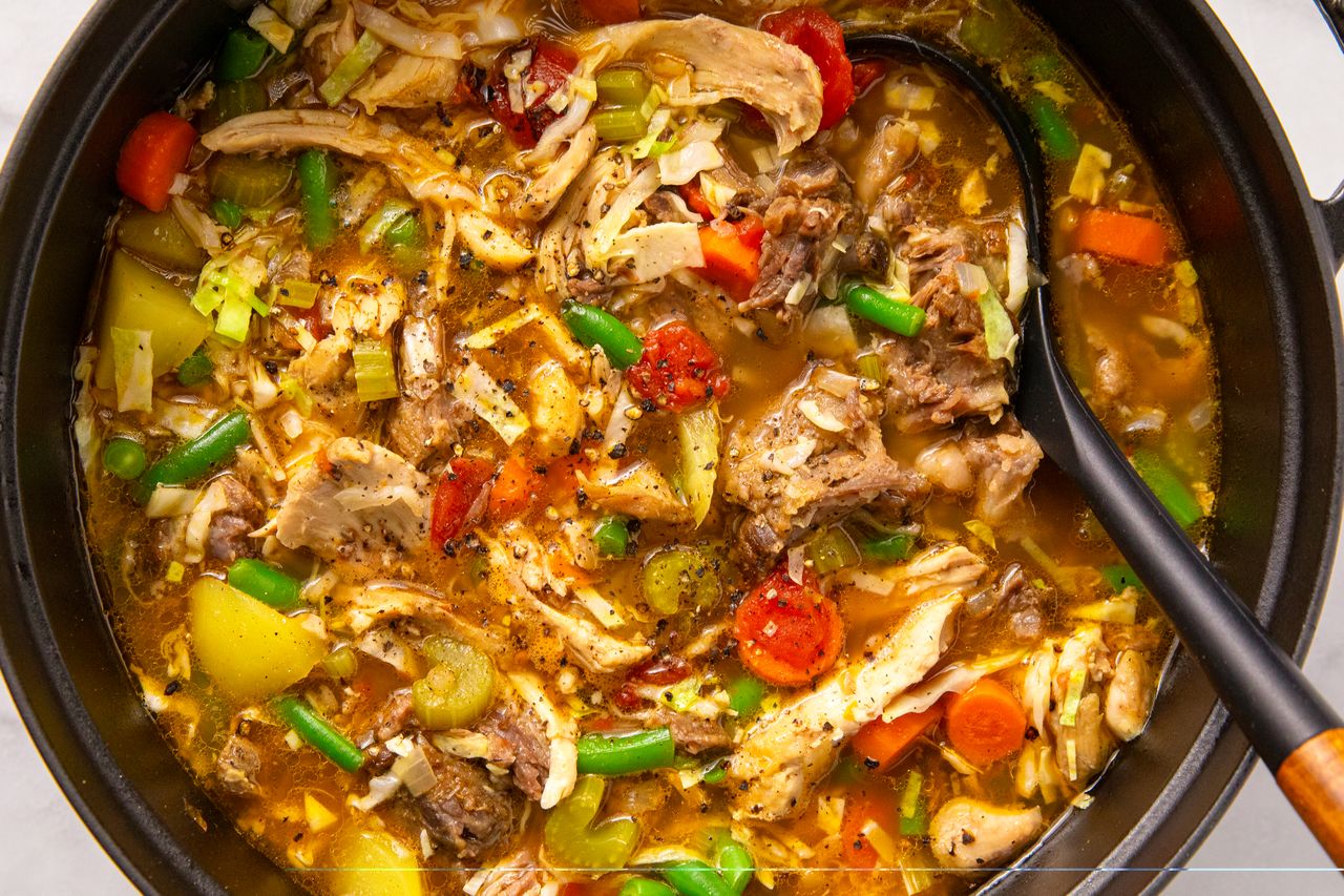 A pot of hearty stew containing assorted vegetables shredded meat and a broth with a ladle resting in the pot