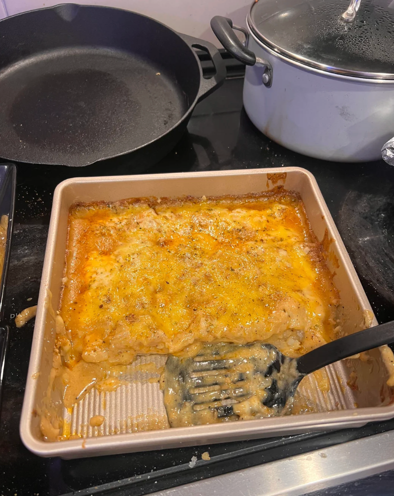 A baking dish with scalloped potatoes on a stovetop, partly served with a spoon in the corner of the dish