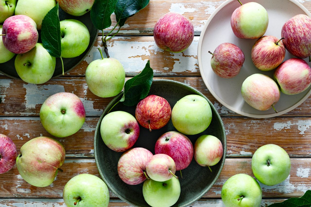 Fresh homegrown apple fruits with leaves on wooden background viewed from above, harvesting still life