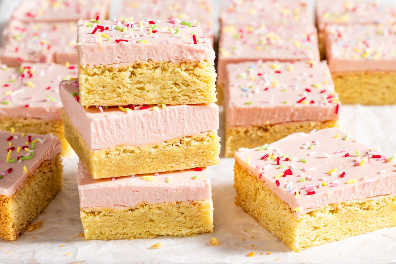 Sugar cookie bars with frosting and sprinkles stacked on parchment paper
