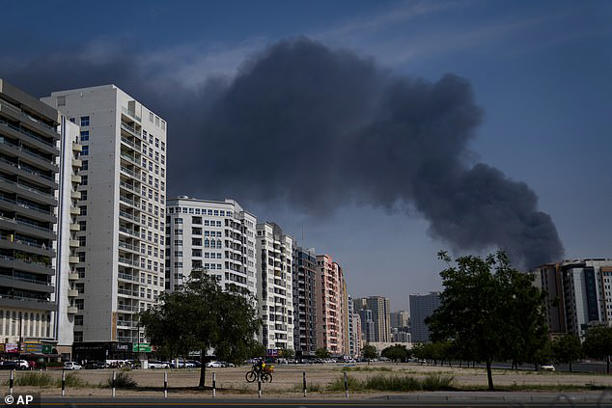 A cyclist rides past as black plume of smoke is seen rising from a warehouse at the industrial area of Sharjah City in the United Arab Emirates