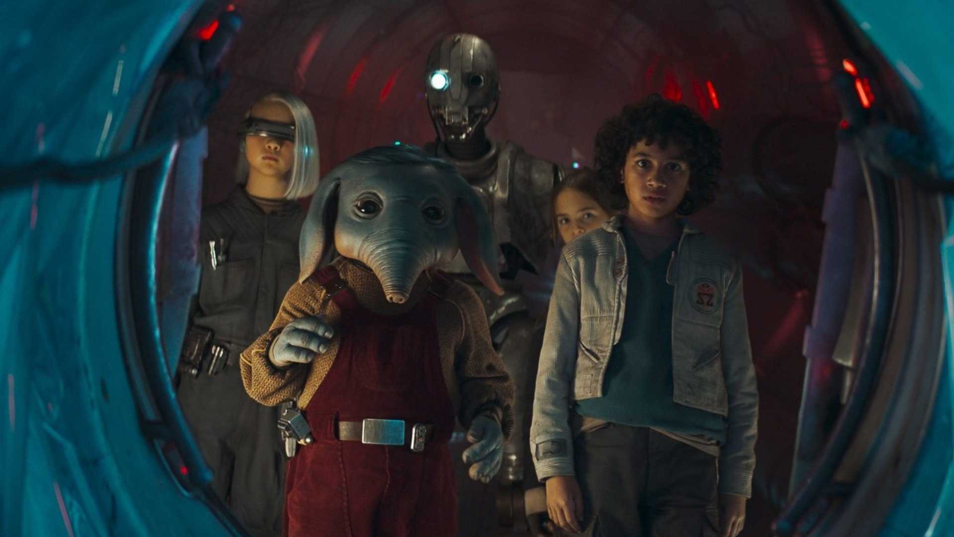 Three children, an elephant-like alien, and a droid behind them peer through a circular hatch from a spaceship.