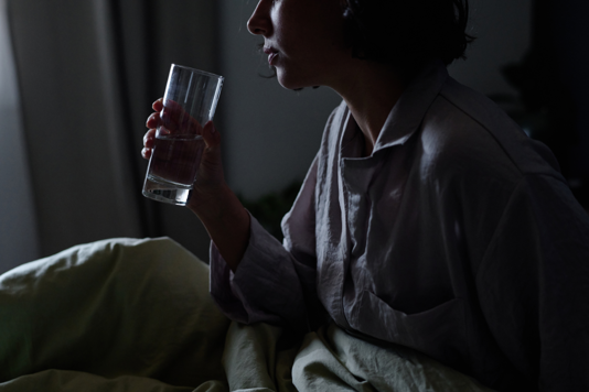 Stock image of a woman holding a glass of water in bed.