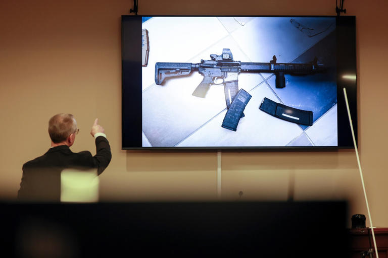 Jason Getz/AP - PHOTO: District Attorney Brad Smith, left, points to a weapon that was displayed on the screen during the first day of the trial of Colin Gray, the father of Apalachee High School shooting suspect Colt Gray, February 16, 2026.