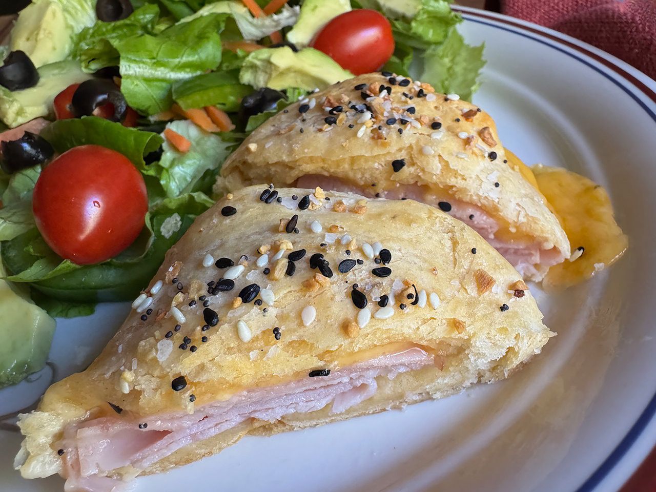 split triangular biscuits filled with ham and cheese, sprinkled with everything seasoning, on plate with green salad