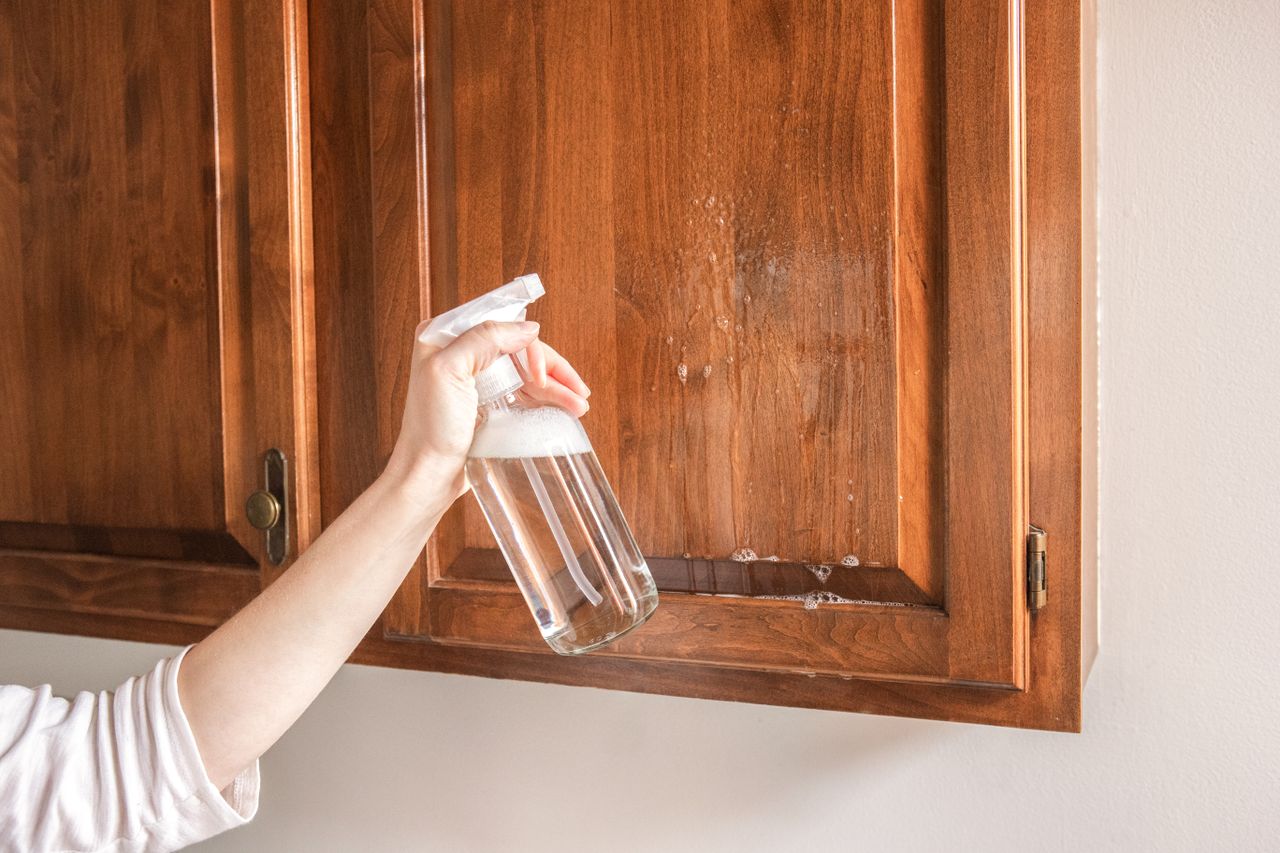Using a spray bottle of vinegar to clean wood kitchen cabinets