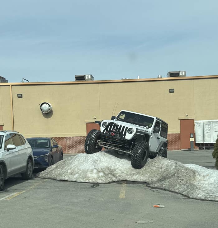A white off-road vehicle parked on a pile of snow in a parking lot, showcasing its rugged capability