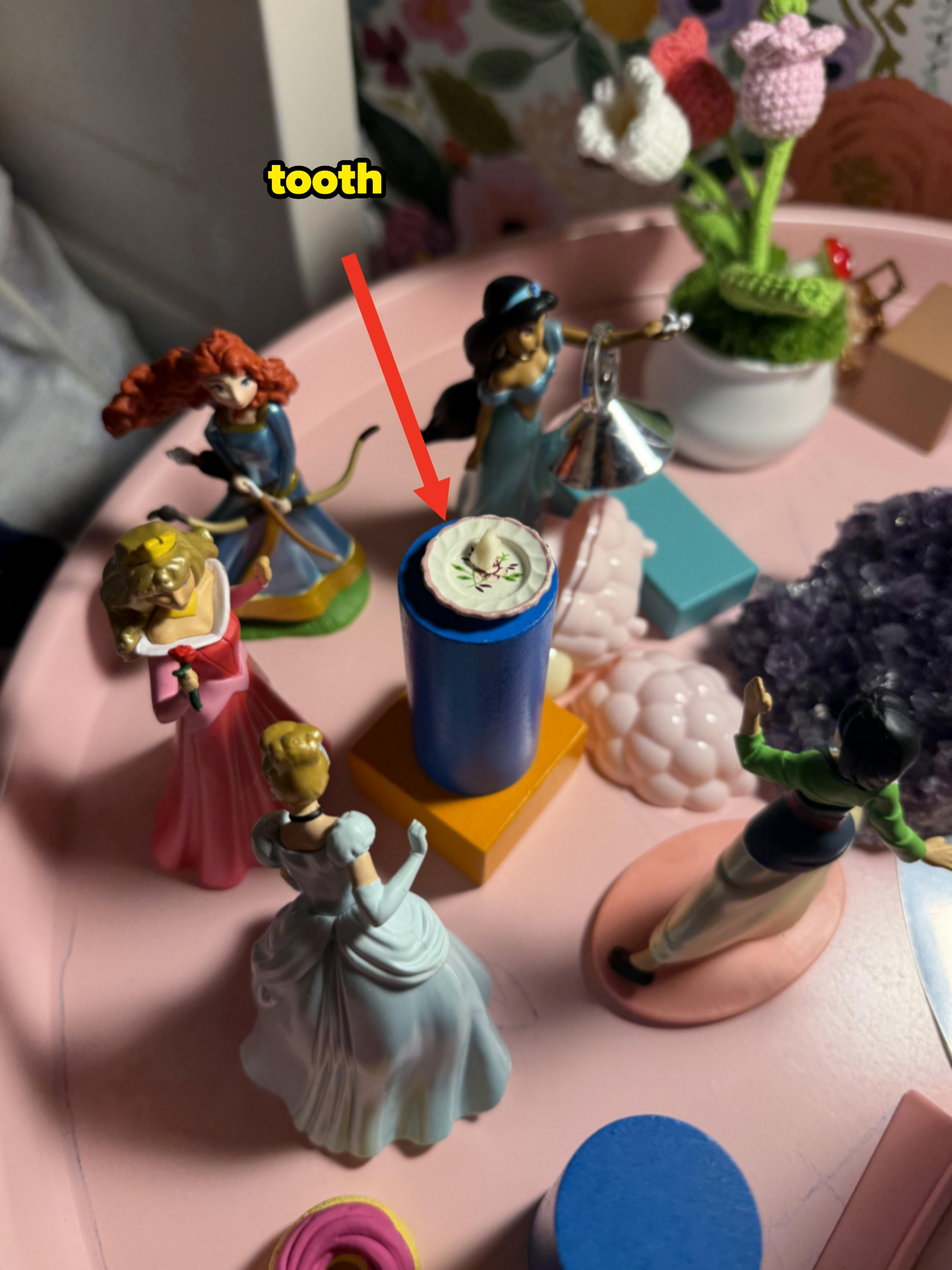 Figurines of fairy-tale characters in gowns and assorted hairstyles are arranged on a table with decorative items