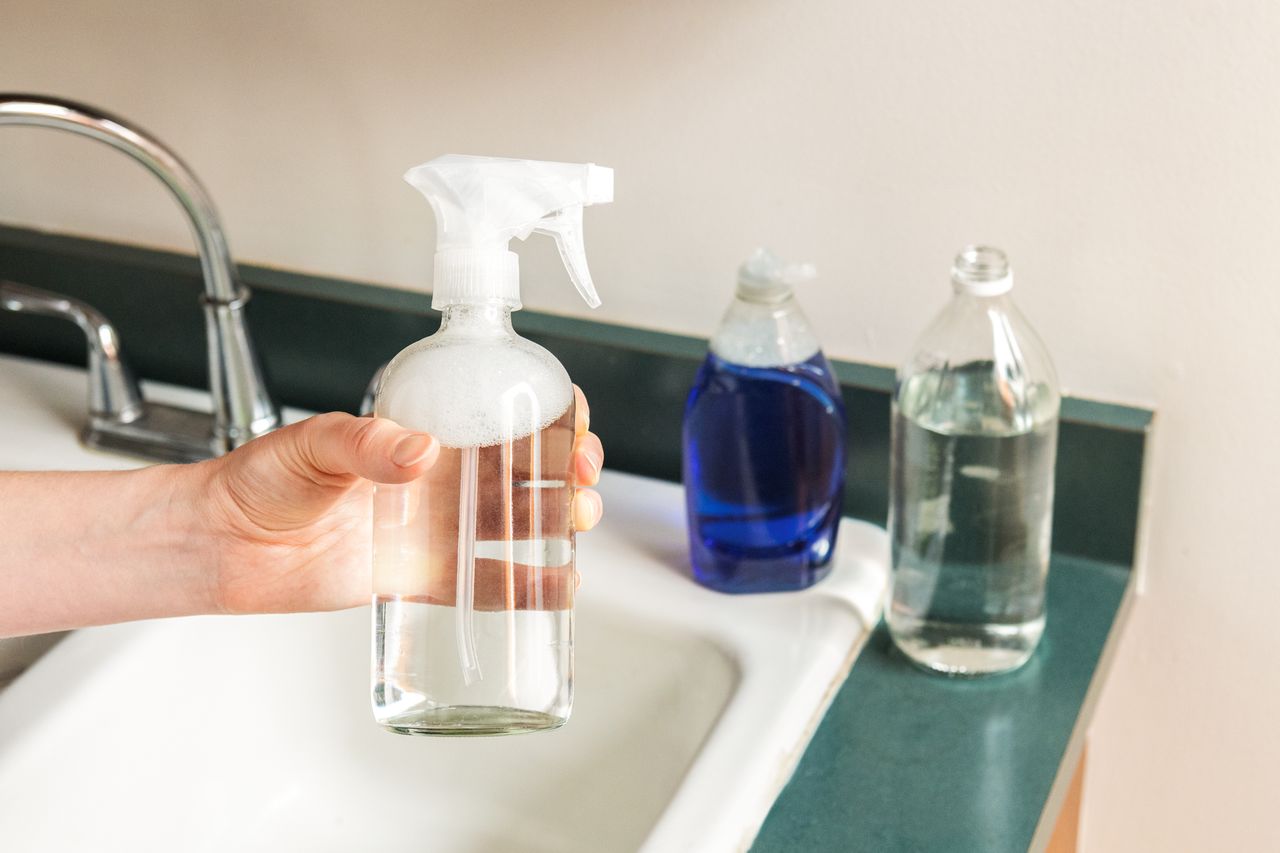 Hand holding a spray bottle of vinegar over sink