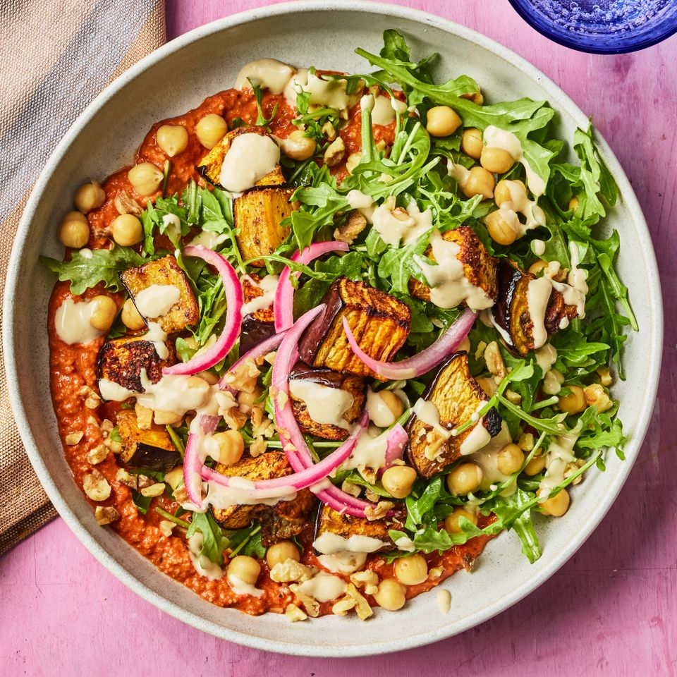 A bowl of food with chickpeas roasted vegetables greens and sauce