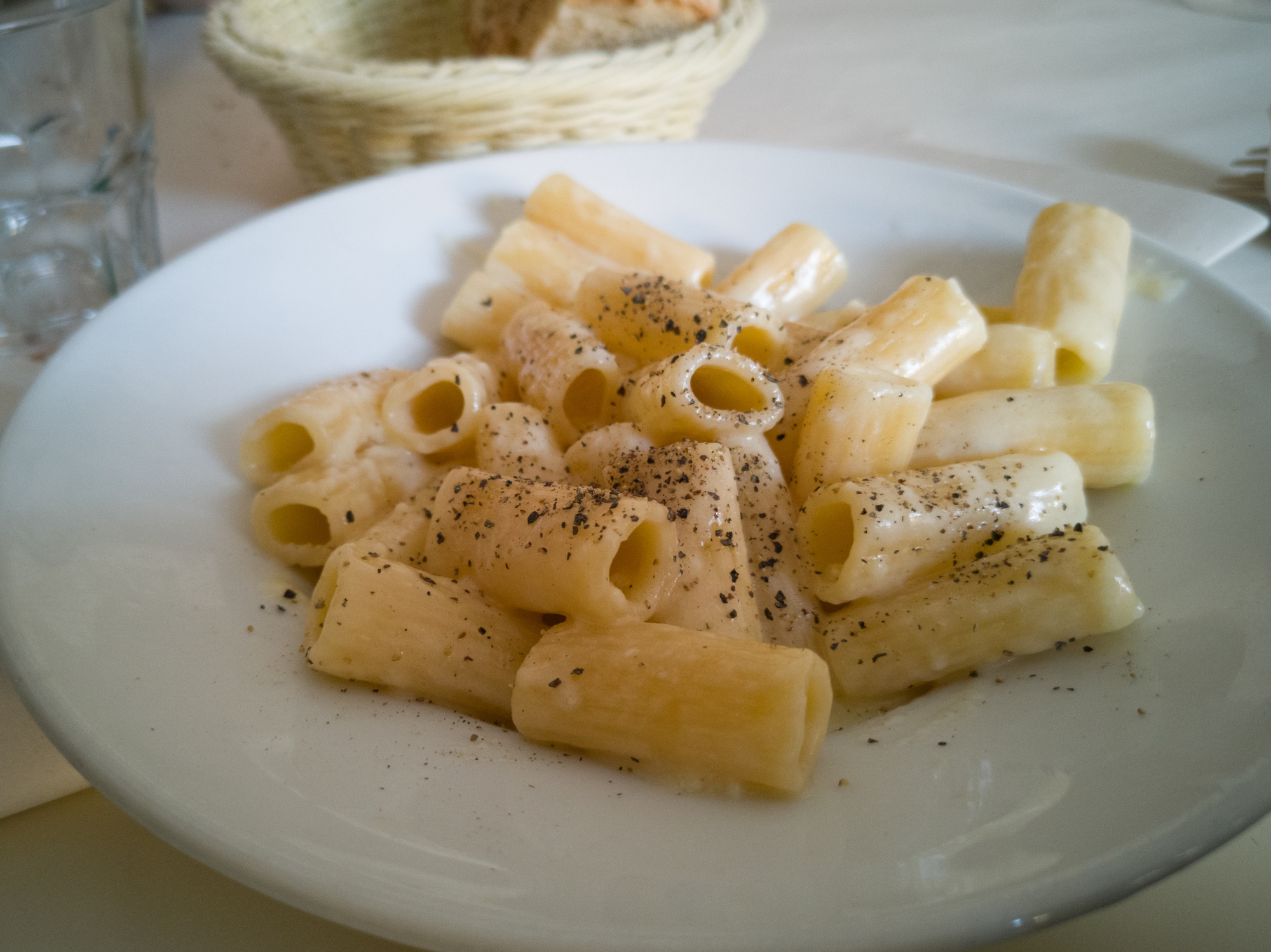 A plate of rigatoni pasta coated in a creamy sauce, topped with freshly ground black pepper, served on a white plate