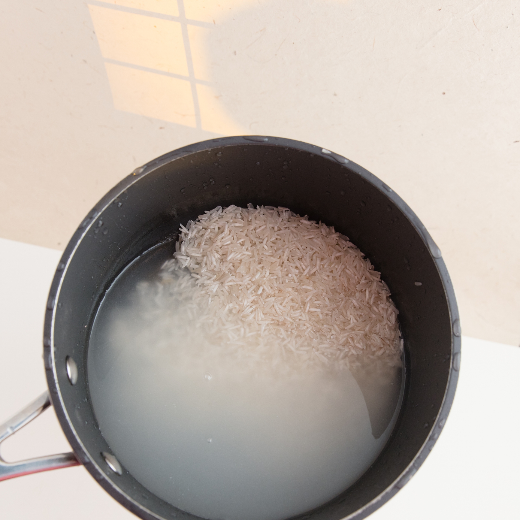 Uncooked rice soaking in water inside a pot, viewed from above, with light casting a window-like shadow on the surface