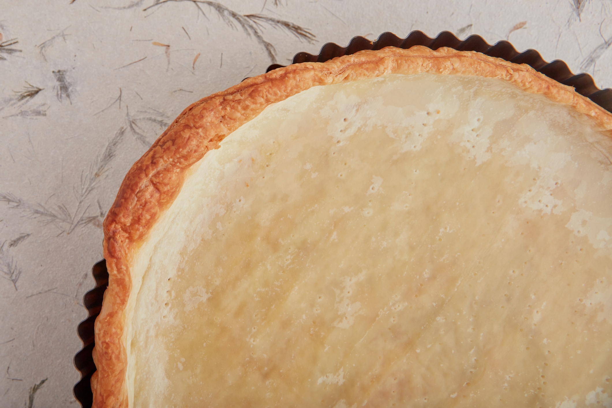 Close-up of a baked pie crust in a dark pan, viewed from above, on a textured background