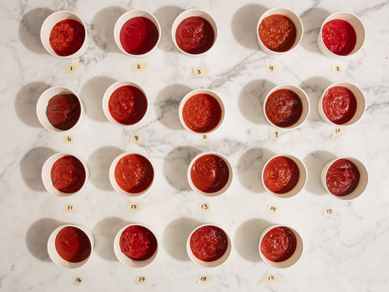 Twenty cups of pizza sauce arranged in rows on a marble surface part of a taste test