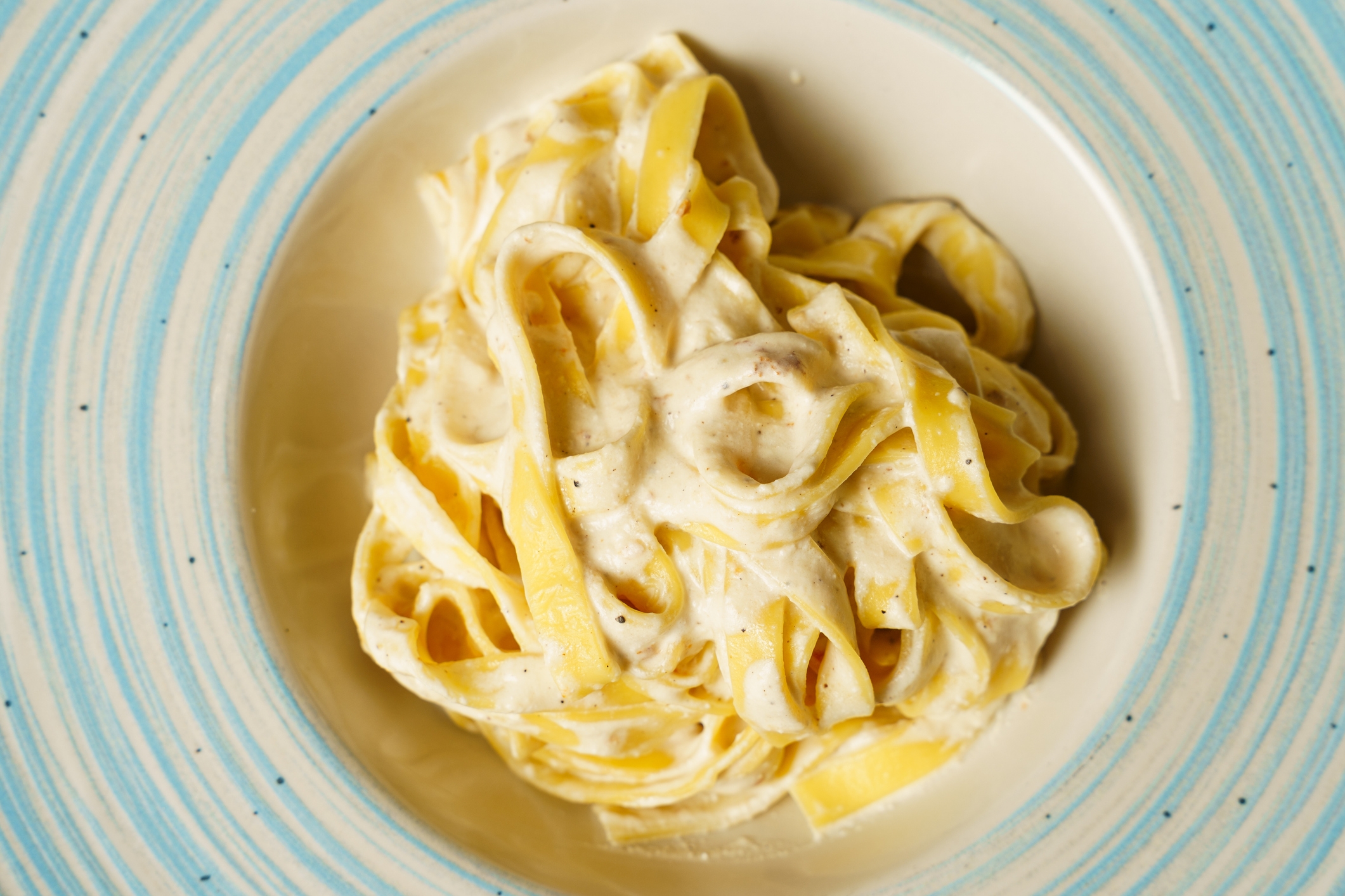 A plate of creamy fettuccine Alfredo pasta, neatly twirled and served on a white dish with decorative lining