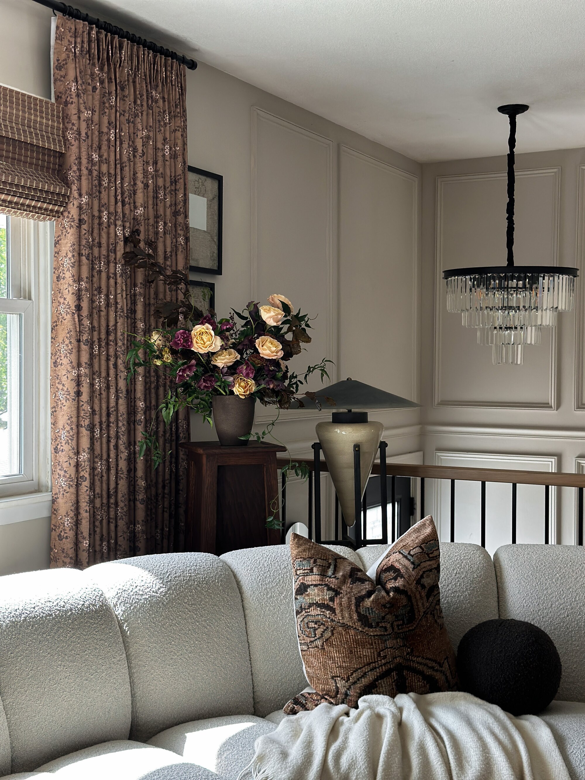 Image of an off-white sitting area with a curved, boucle sofa in the foreground. There is a window on the right wall that has both a roman blind and a patterned curtain on it.