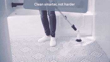 Person cleaning a tiled bathroom floor with an electric scrubber. Text reads,
