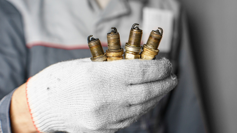 A mechanic holding four old, used spark plugs with a gloved hand