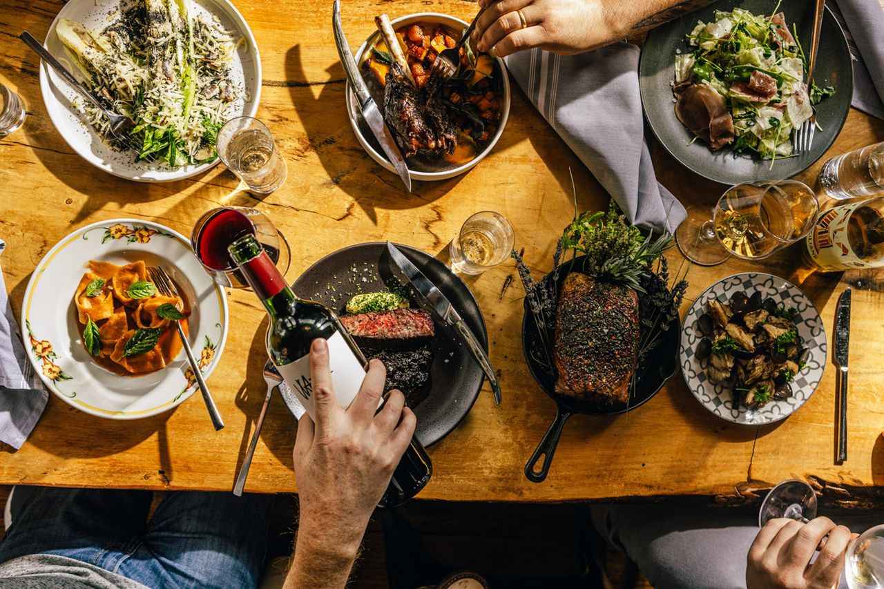 A table with a variety of dishes and a person pouring wine