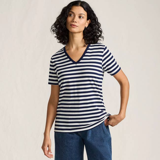 Person wearing a striped V-neck shirt and jeans, posing casually. The image is part of a shopping article