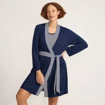 Person wearing a stylish knee-length robe with a striped belt and inner lining, posing against a plain backdrop