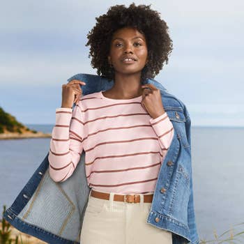 Person by a beach in a striped shirt and denim jacket, embodying a casual fashion style suitable for a shopping-focused article