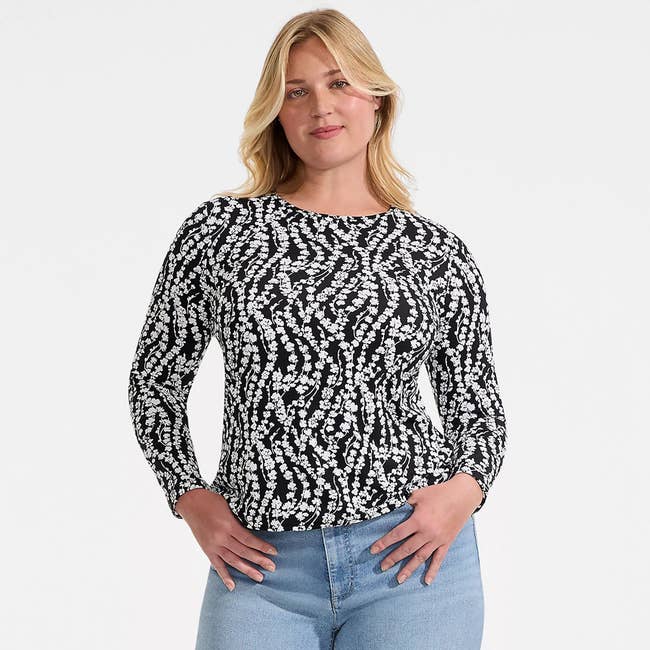 Person in a black and white patterned long-sleeve top and blue jeans, posing confidently