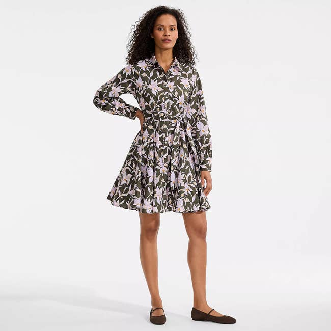 Person wearing a floral-patterned, long-sleeve dress with a flared skirt and flats, standing in a neutral pose