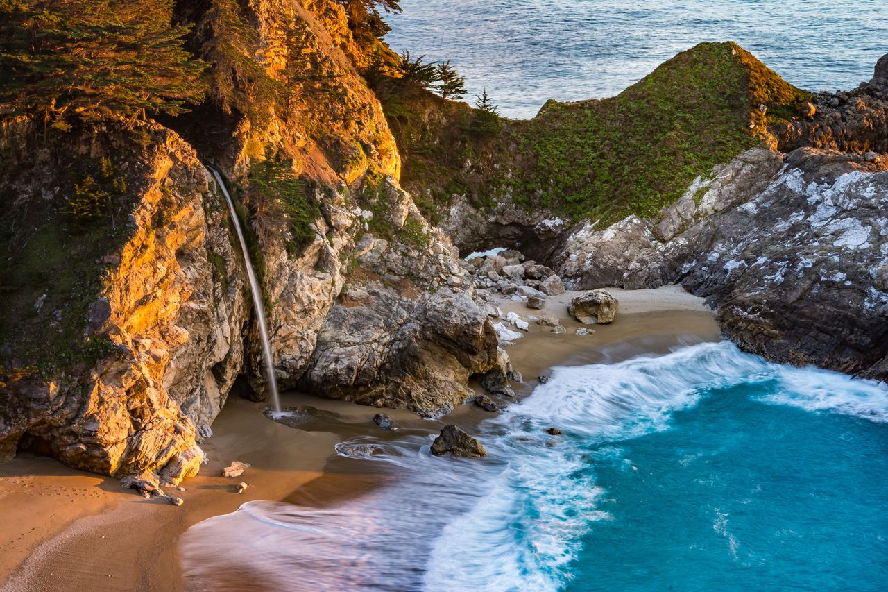 McWay Falls cascading onto a sandy beach bordered by rocky cliffs and a turquoise sea located in Julia Pfeiffer Burns State Park