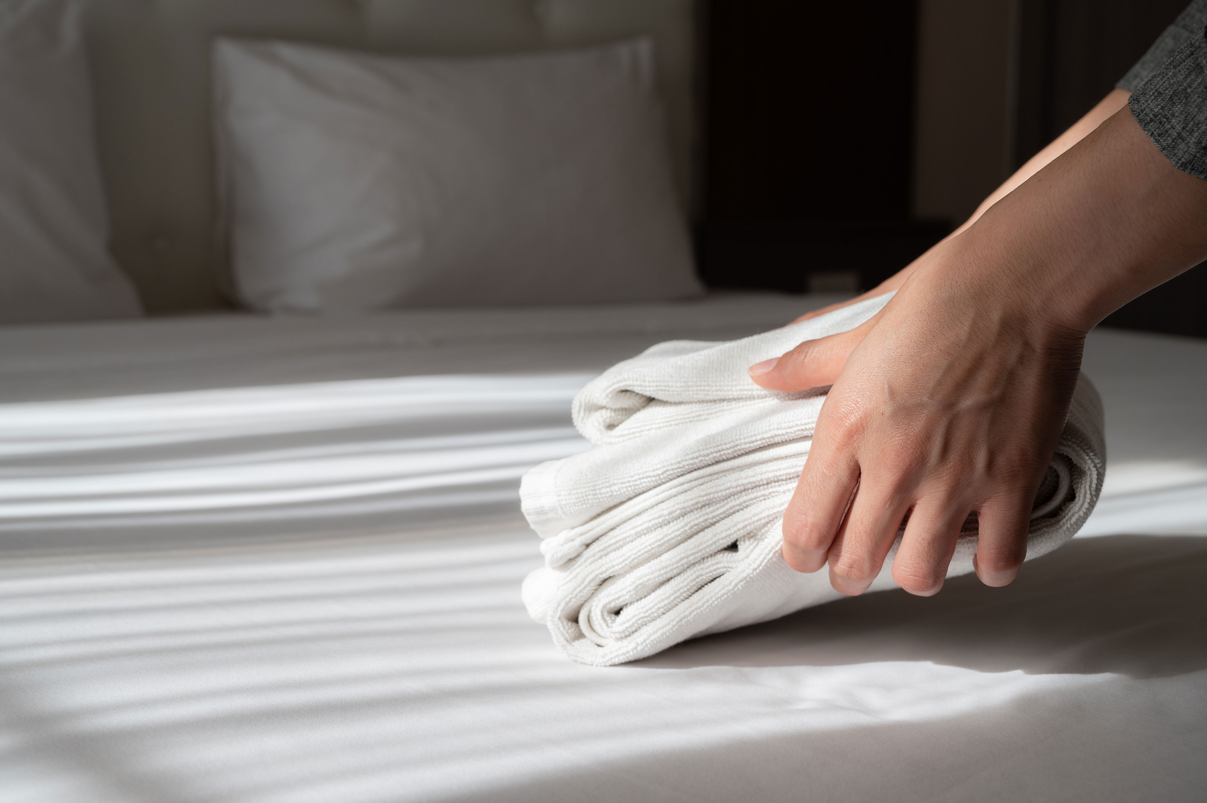 Hands placing folded towels on a neatly made bed