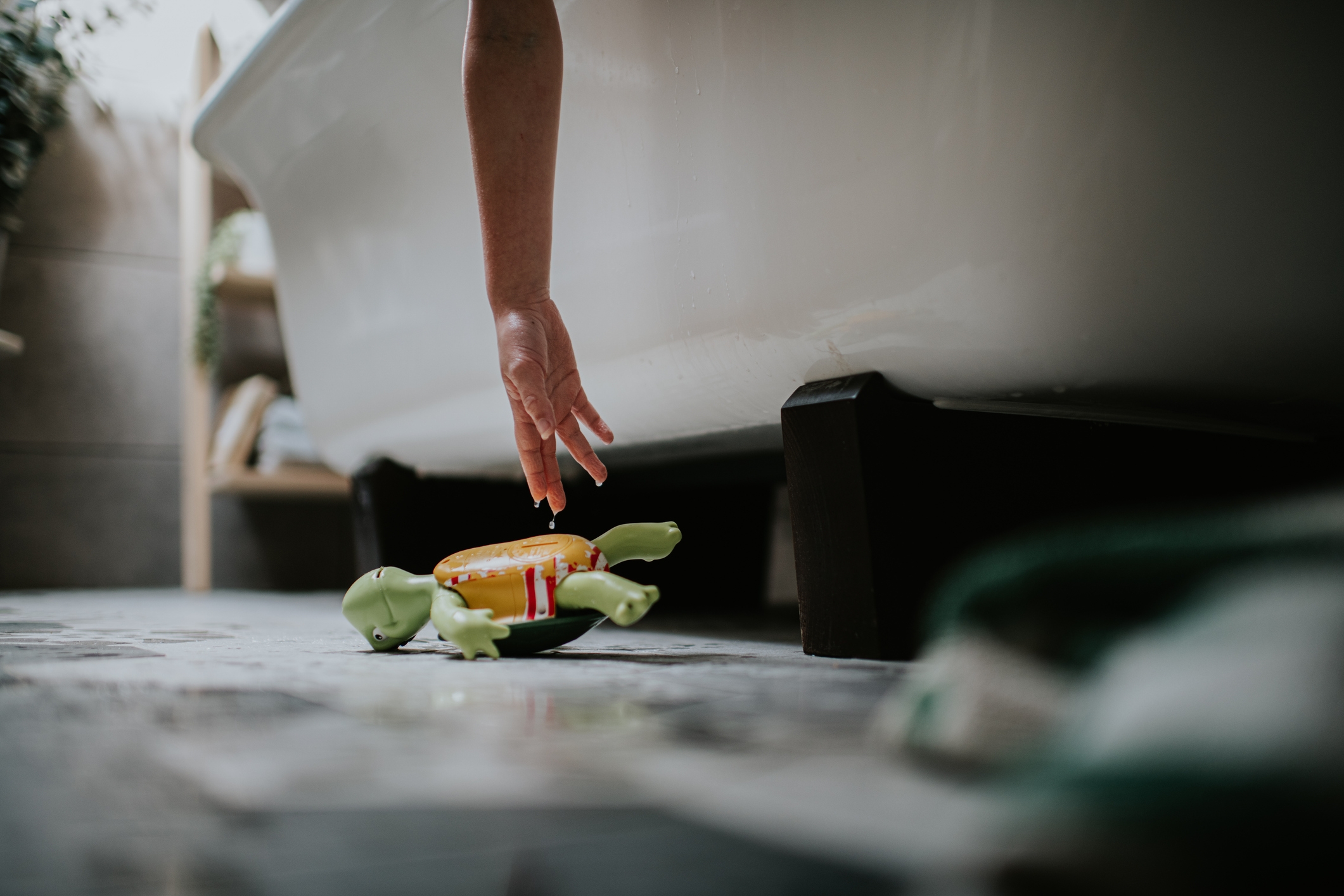 Hand reaching from bathtub to a bath toy floating on the water, creating a playful and relaxing atmosphere
