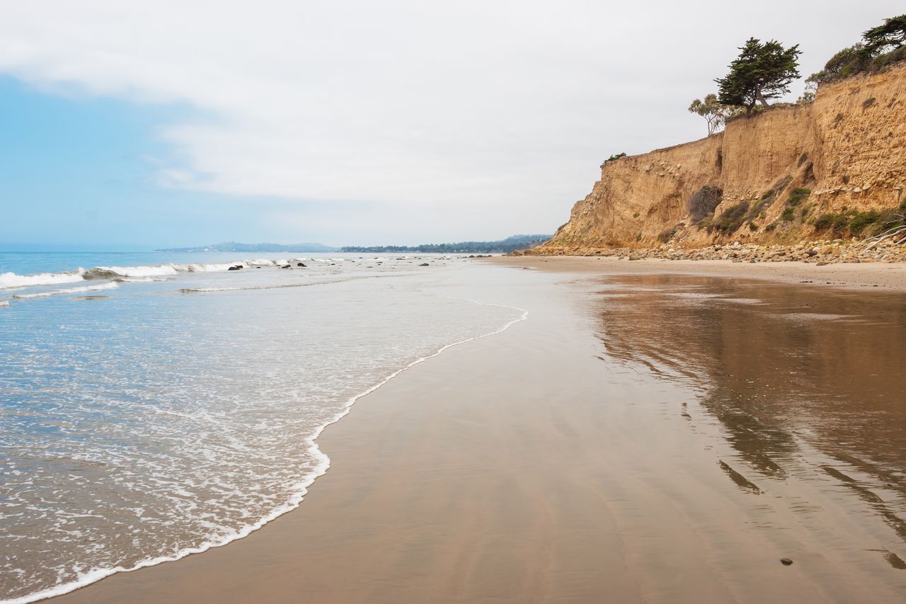 A serene beach with cliffs and ocean waves in the background featuring a wide open shoreline