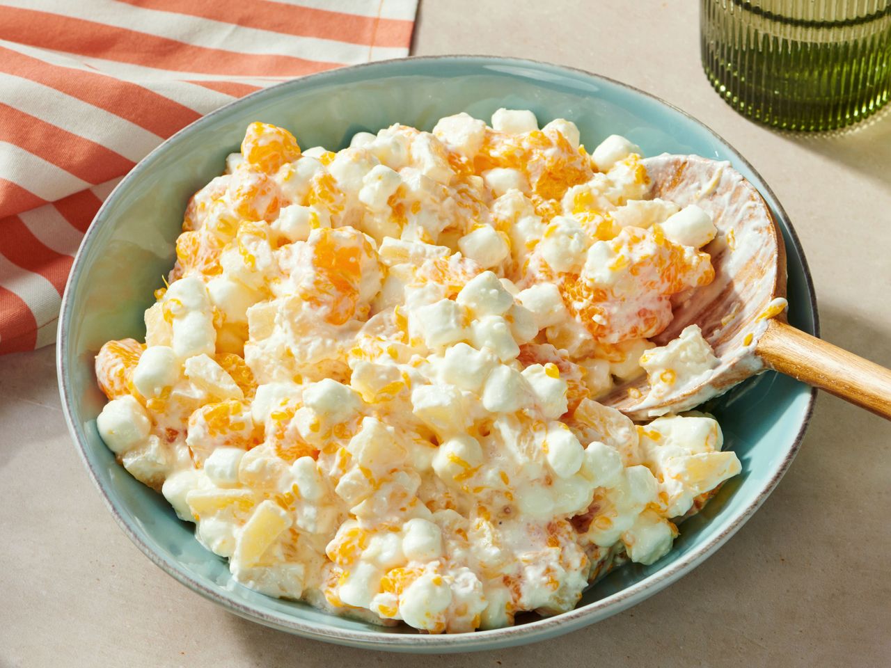 A bowl of ambrosia fruit salad with a wooden spoon