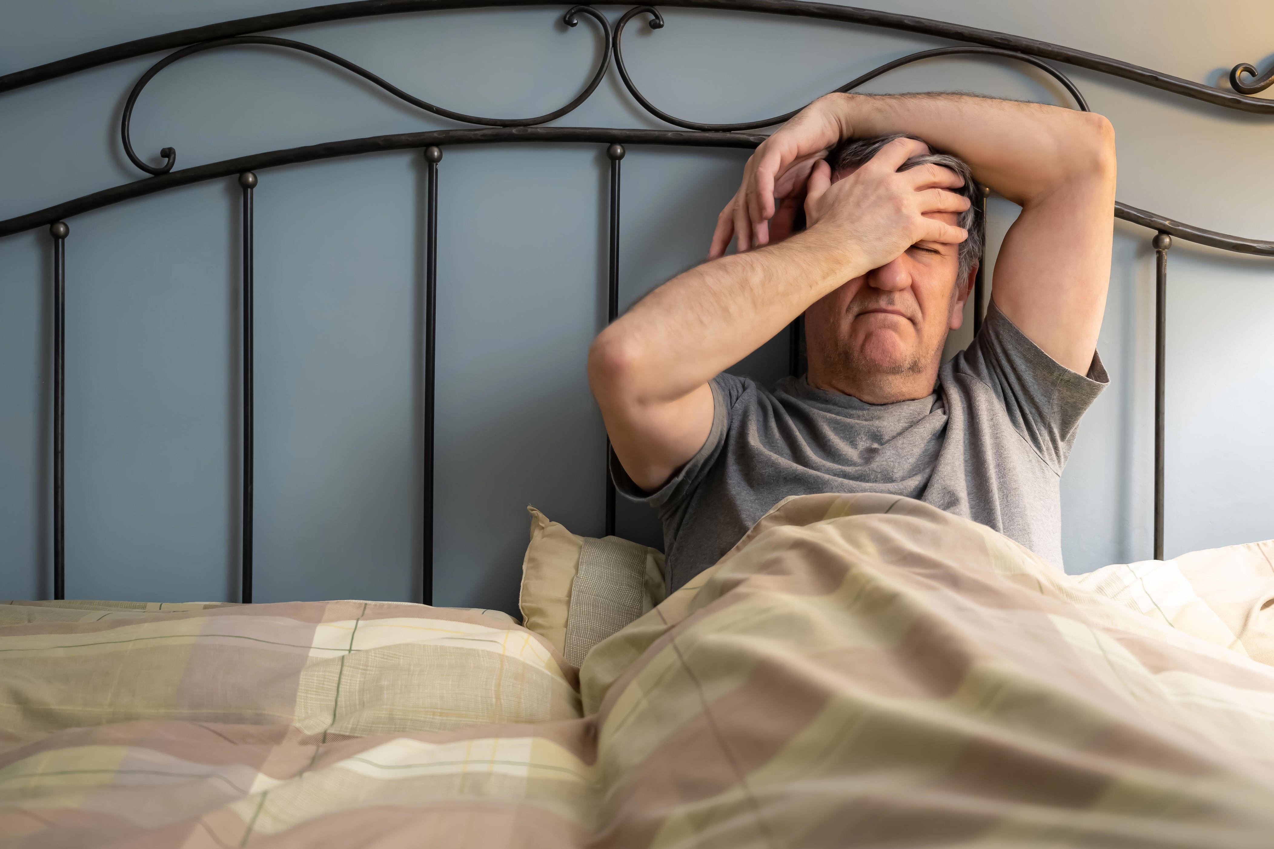 Man with insomnia sitting up in bed with a gesture of despair.