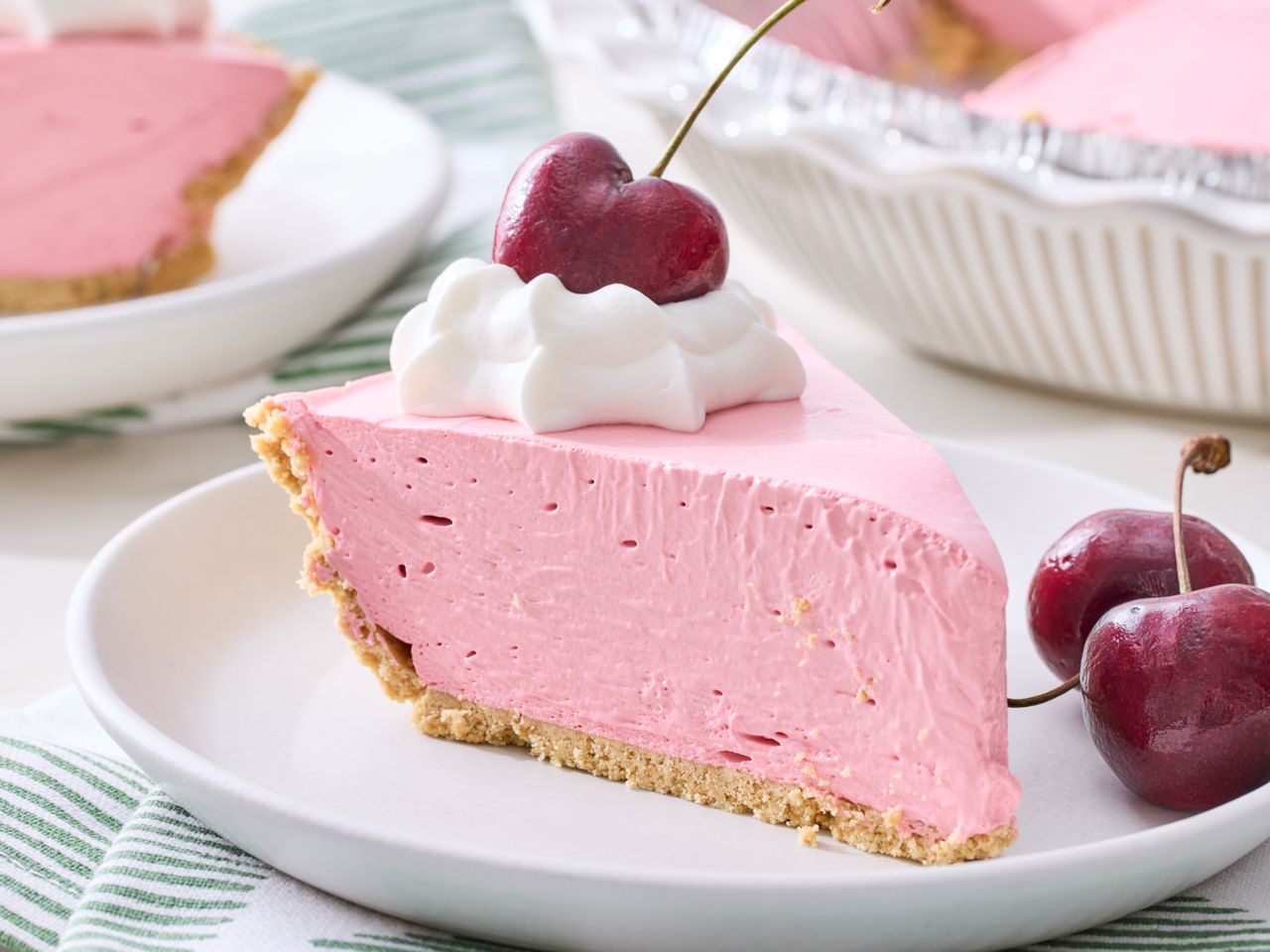 Slice of pink Kool-Aid pie with whipped cream and cherries on a plate