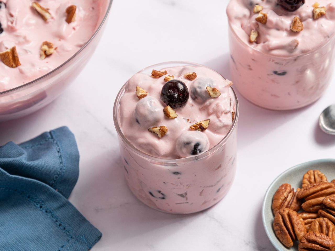 Glass of creamy cherry salad with pecans on a blue surface.