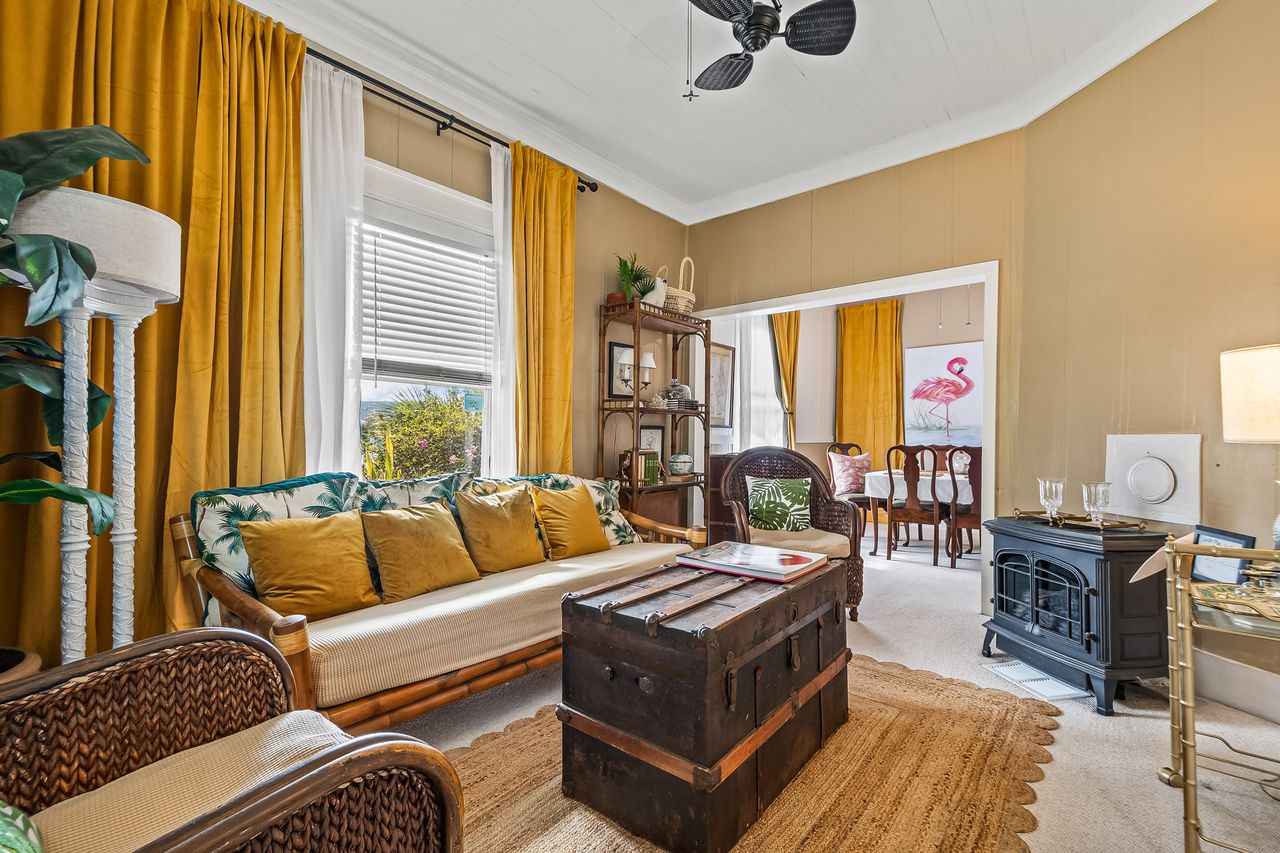 Living area in a vintage style yellow curtains a sofa chairs and a trunk table decorative objects on shelves doorway to a dining area