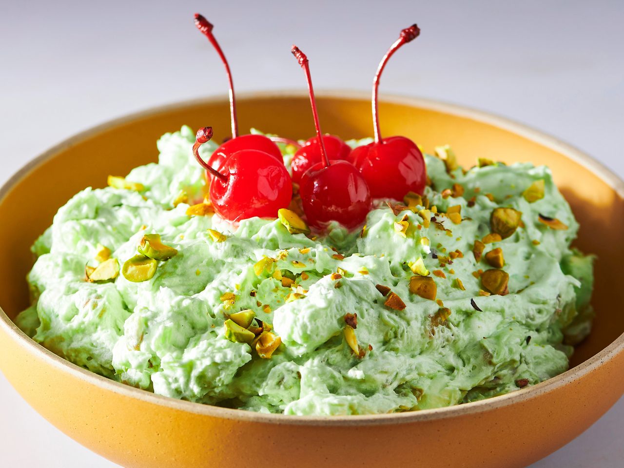 A bowl of Watergate salad topped with maraschino cherries and sprinkled with chopped nuts, presenting a vibrant green hue typical of the dessert.