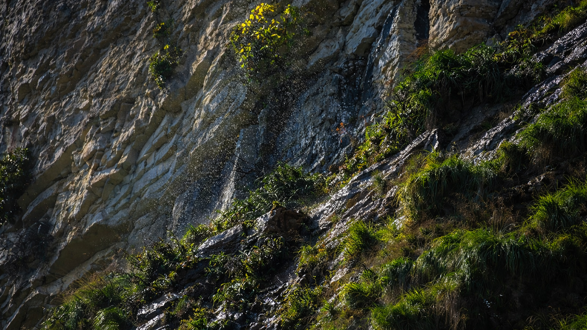 A hidden spring dripping down a sunlit mountain cliff