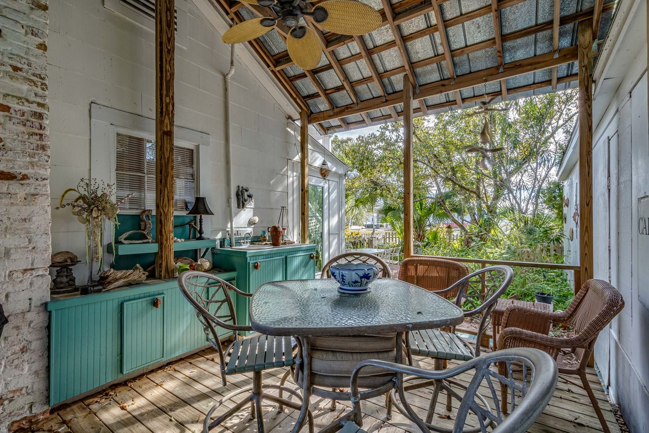 A covered porch featuring a table and chairs surrounded by cabinets and overlooking foliage